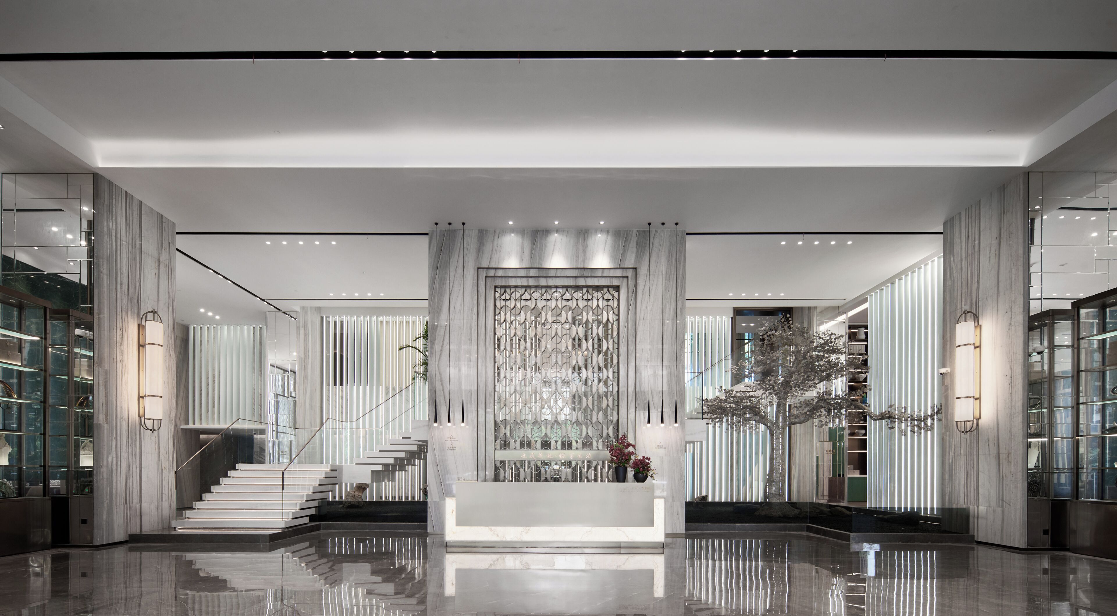 A modern lobby with a central staircase, marble walls, and a decorative wall panel.