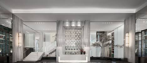 Un vestíbulo moderno con una escalera central, paredes de mármol y un panel decorativo.