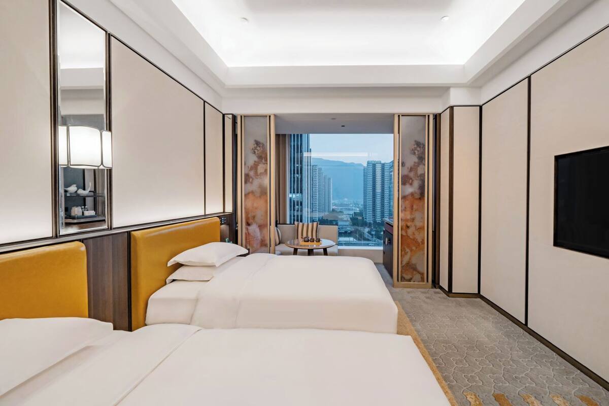 Une chambre d’hôtel avec deux lits, un canapé, une télévision et une vue sur la ville.