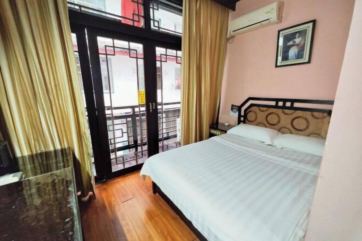 A hotel room with a bed, curtains, an air conditioning unit, and a window with a view.