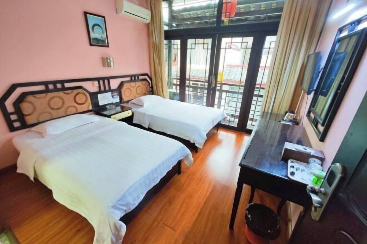 A hotel room with two beds, a desk, a television, and a view through a glass door.