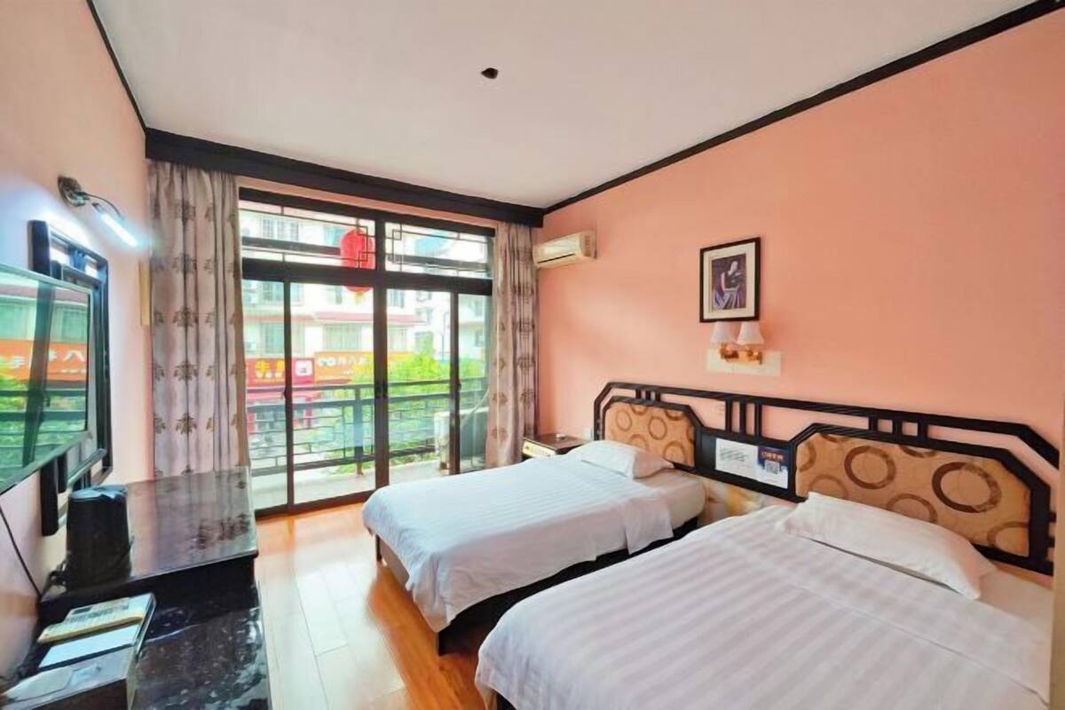A hotel room with two beds, a desk, a TV, and a balcony with a view.