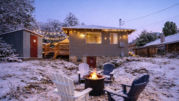 Ein gemütliches Blockhaus mit Feuerstelle und Adirondack-Stühlen in einem verschneiten Garten.