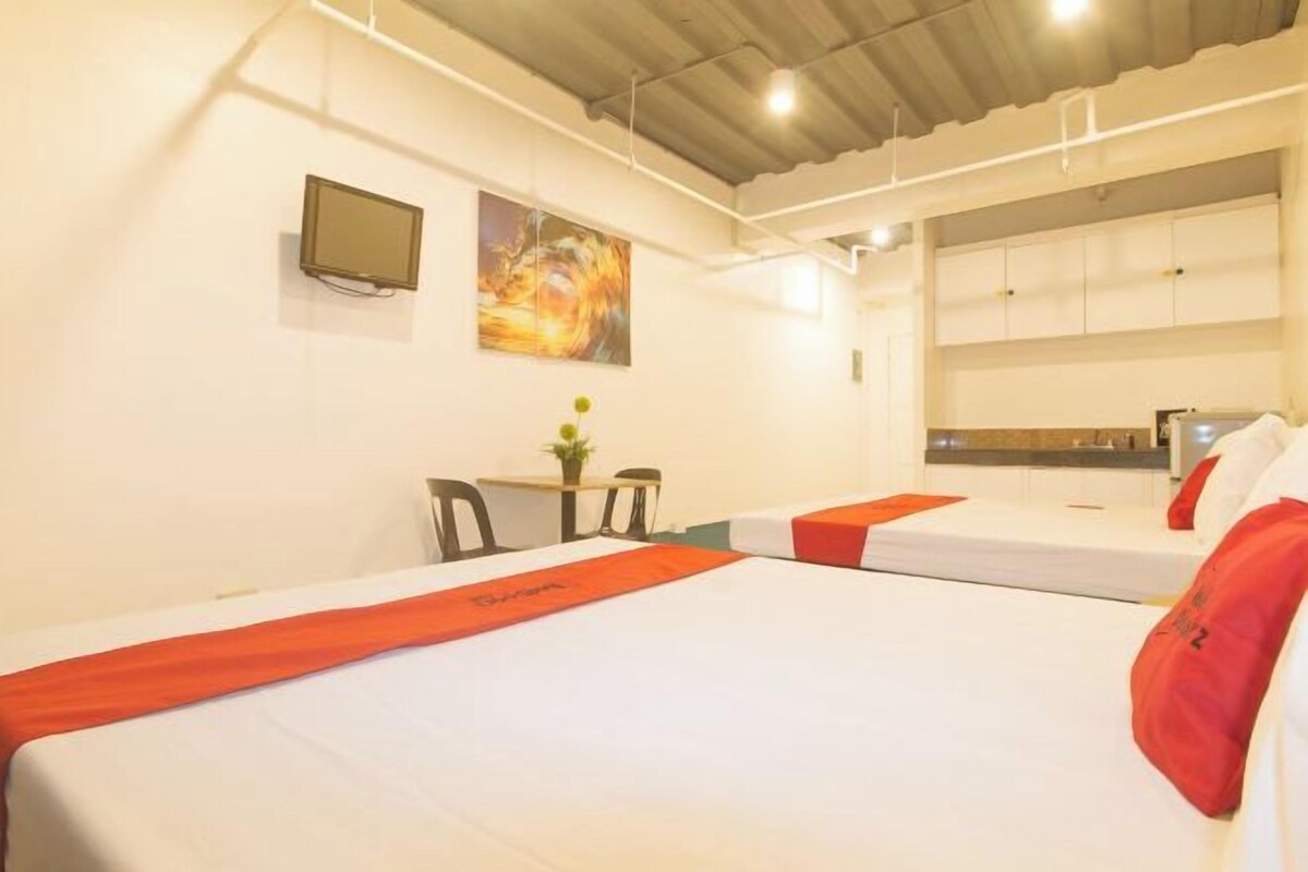 A hotel room with two beds, a desk, a chair, a TV, and a painting on the wall.