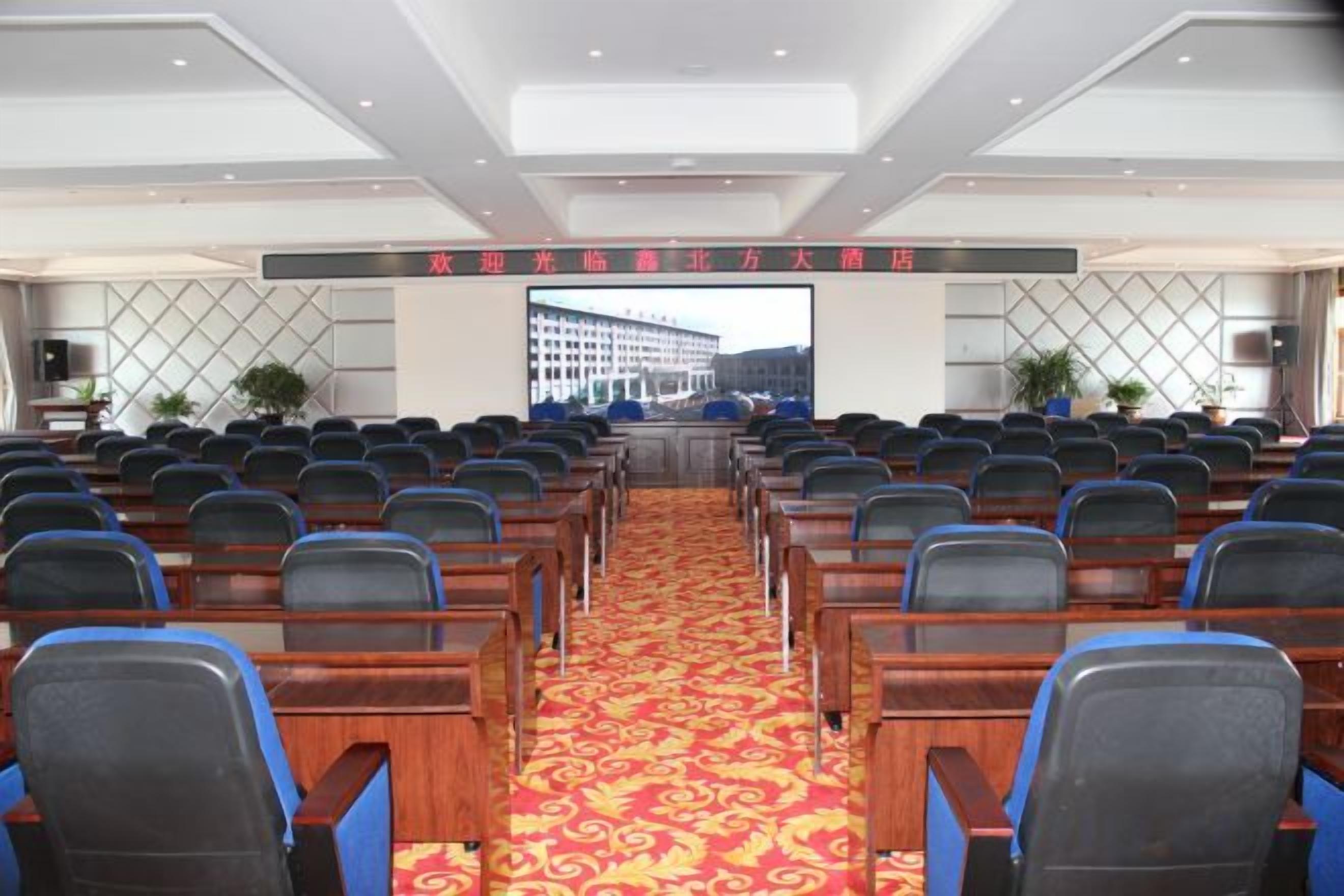 A conference room with rows of chairs, a carpeted floor, and a large screen at the front.