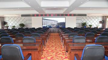 A conference room with rows of chairs, a carpeted floor, and a large screen at the front.