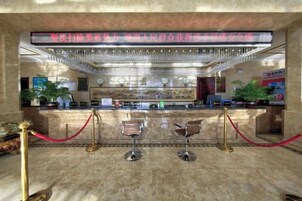 Zona de recepción de un hotel con suelo de mármol, mostrador de recepción, dos taburetes de bar, una barrera de cuerda roja y una araña.