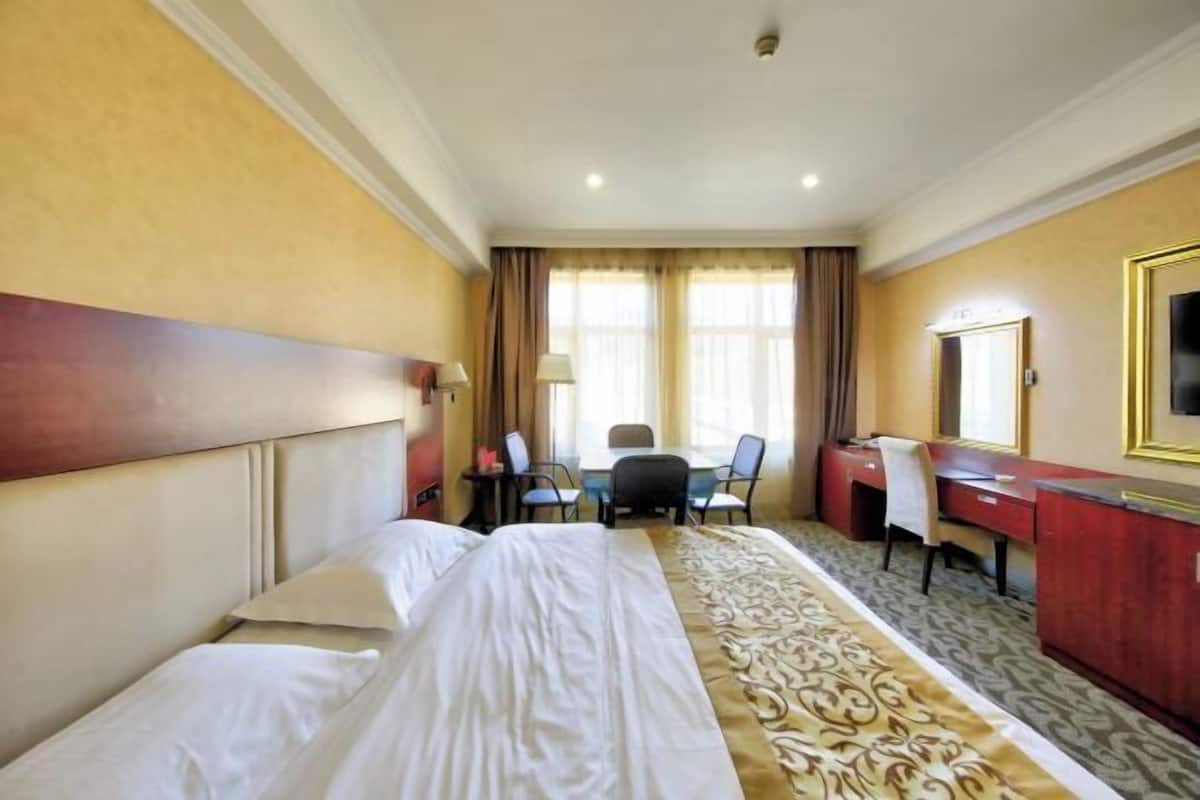 Una habitación de hotel con cama, escritorio, silla y un espejo grande.