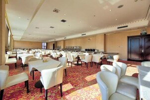 Un gran salón de banquetes con varias mesas y sillas, una zona de cocina y un mostrador de recepción.