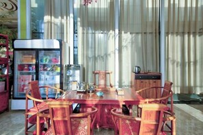 A dining area with a wooden table and chairs, a refrigerator, and a window with curtains. - Jinyou Hotel (Liuhe)