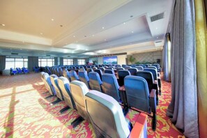Une salle de conférence avec des rangées de chaises, un sol recouvert de moquette et un grand écran à l’avant.