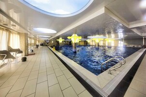 Una piscina interior con suelo de baldosas, una escalera de piscina y un techo con tragaluces circulares.