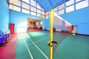 Un gimnasio interior con una red de voleibol, una zona de asientos y una escalera que lleva a un nivel superior.