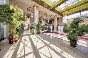 A spacious lobby with large potted plants, marble flooring, and a high ceiling with intricate designs. - Jinyou Hotel (Liuhe)