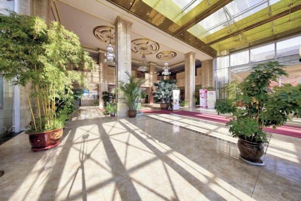 Un hall d’entrée spacieux, agrémenté de grands pots de plantes, doté d’un sol en marbre et d’un plafond élevé orné de motifs complexes.