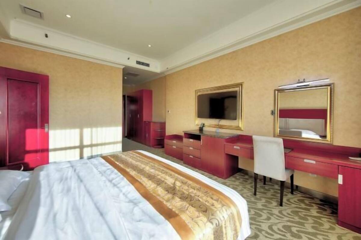 Una habitación de hotel con cama, escritorio, silla, espejo y armario.