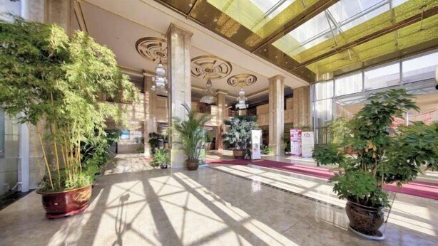 Un hall d’entrée spacieux, doté d’un haut plafond, de grandes colonnes et de plantes en pot.