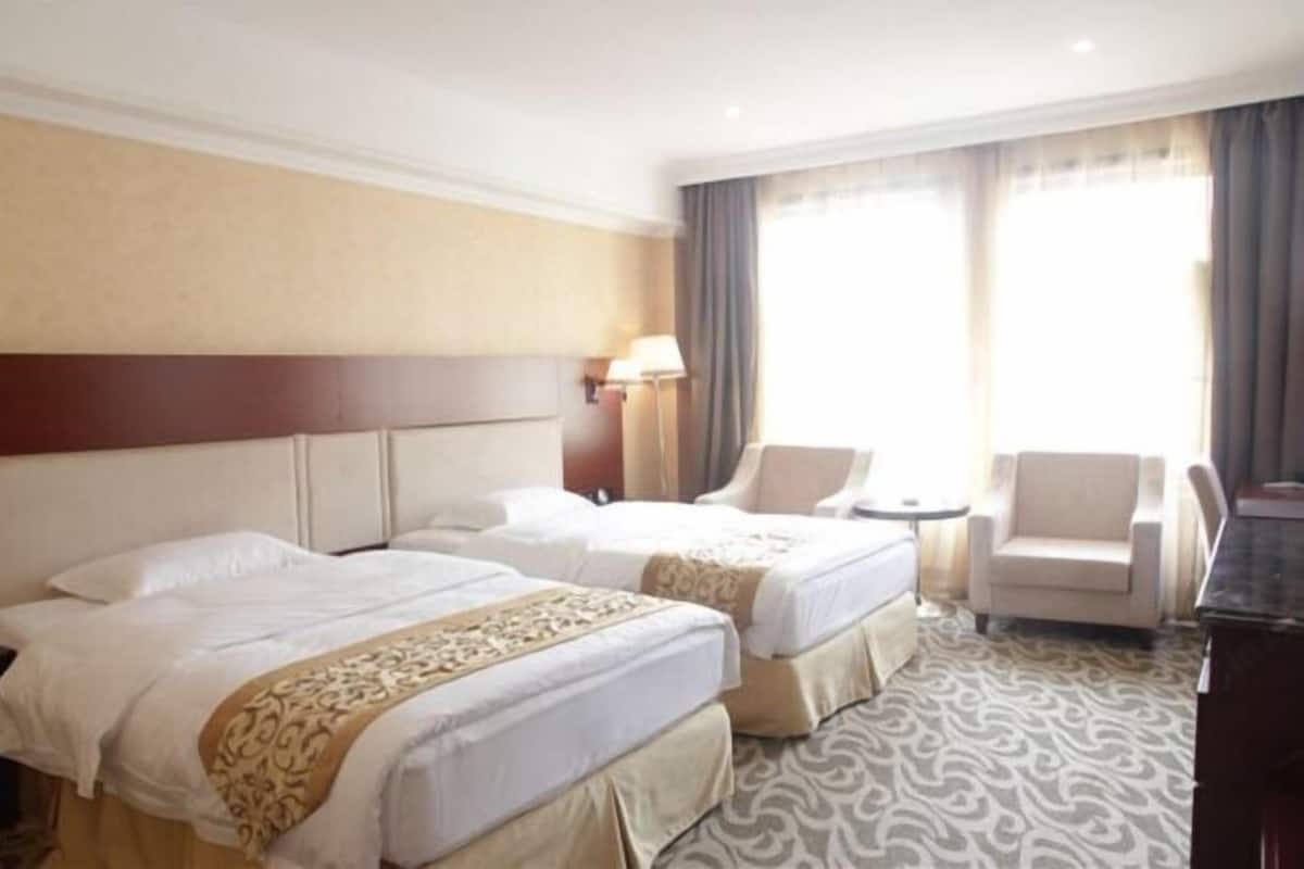 Habitación de hotel con dos camas, un escritorio, una silla y una lámpara.