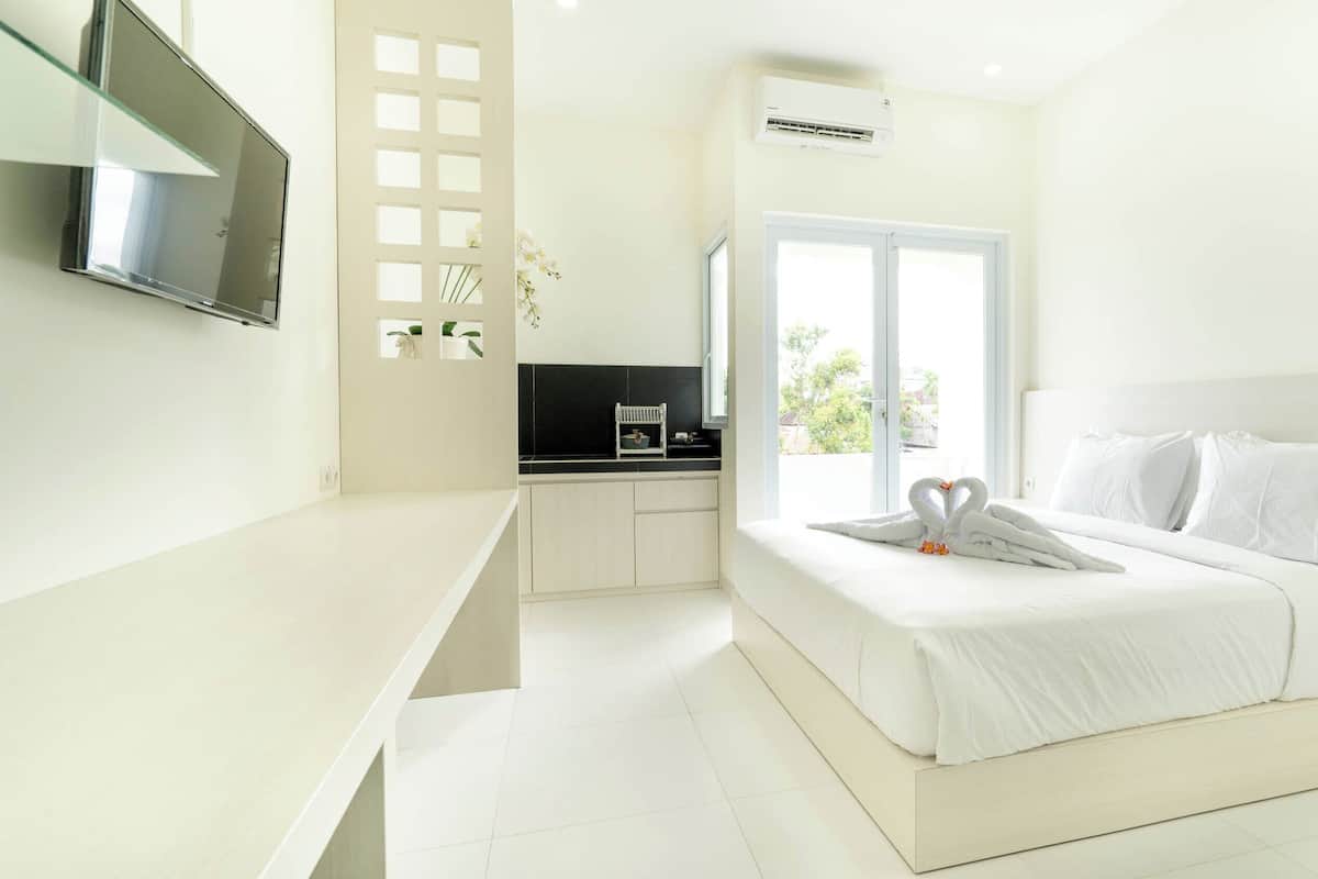 Una habitación de hotel moderna con una cama grande, un televisor montado en la pared, una zona de cocina y un ventanal con vistas al exterior.