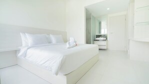 A modern, minimalist bedroom with a large bed, white bedding, and a neatly made towel. - The Axara Bali (Jimbaran)
