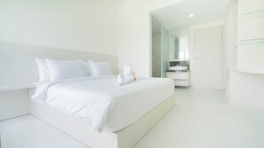 Een moderne, minimalistisch ingerichte slaapkamer met een groot bed, witte beddengoed en een netjes opgevouwen handdoek.