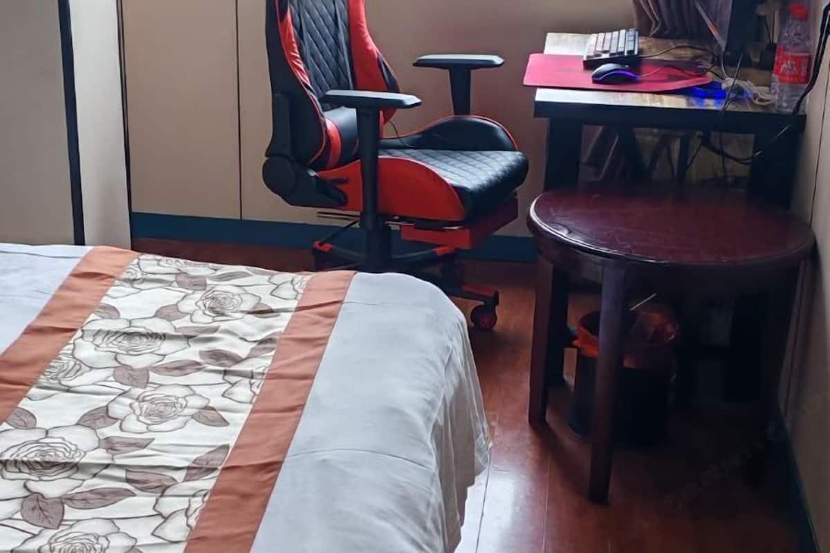 A hotel room with a bed, a desk, a chair, and a small stool.