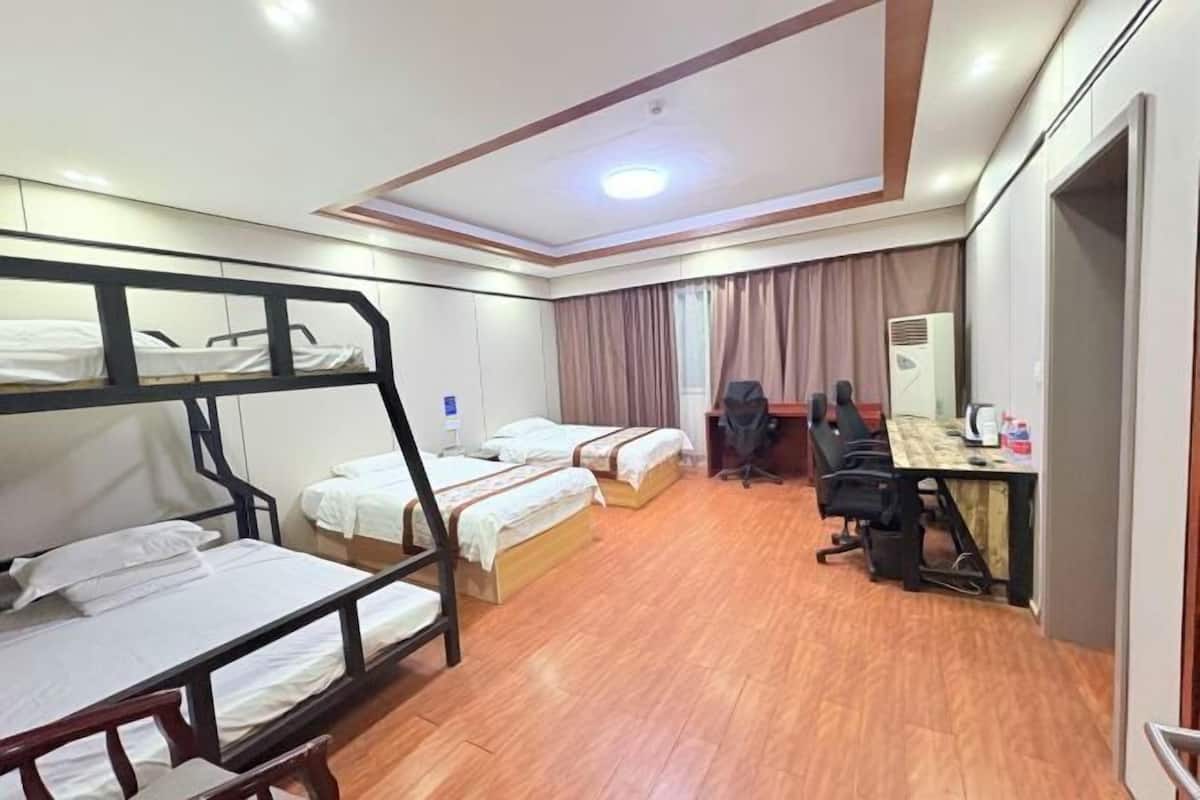 A hotel room with bunk beds, a desk, chairs, a computer, and an air conditioning unit.