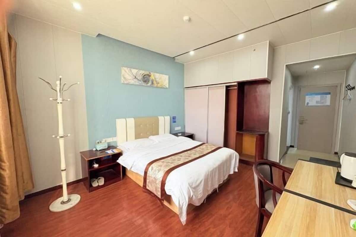 A hotel room with a bed, bedside table, lamp, and a desk with a chair.