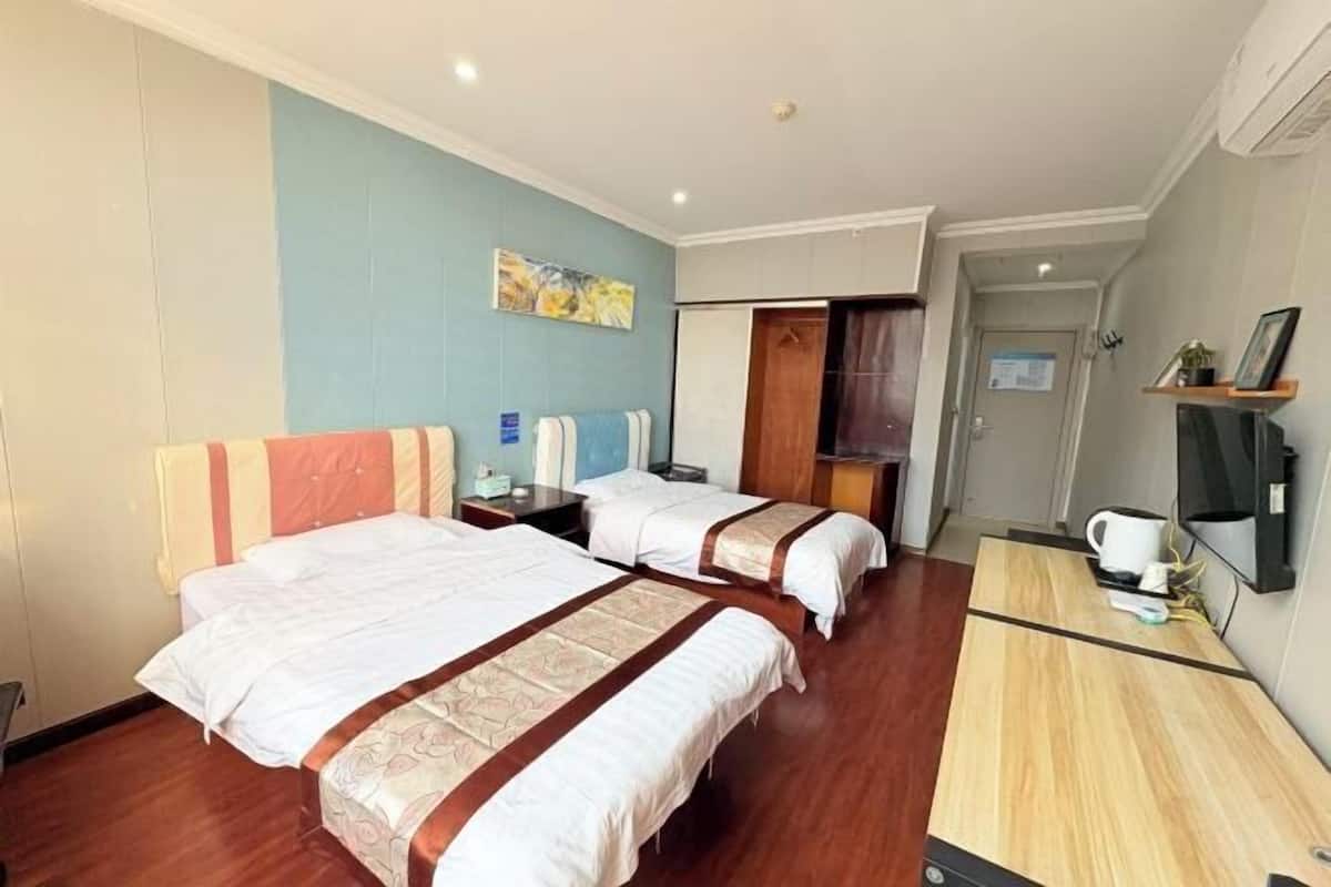 A hotel room with two beds, a wooden desk, a TV, and a painting on the wall.