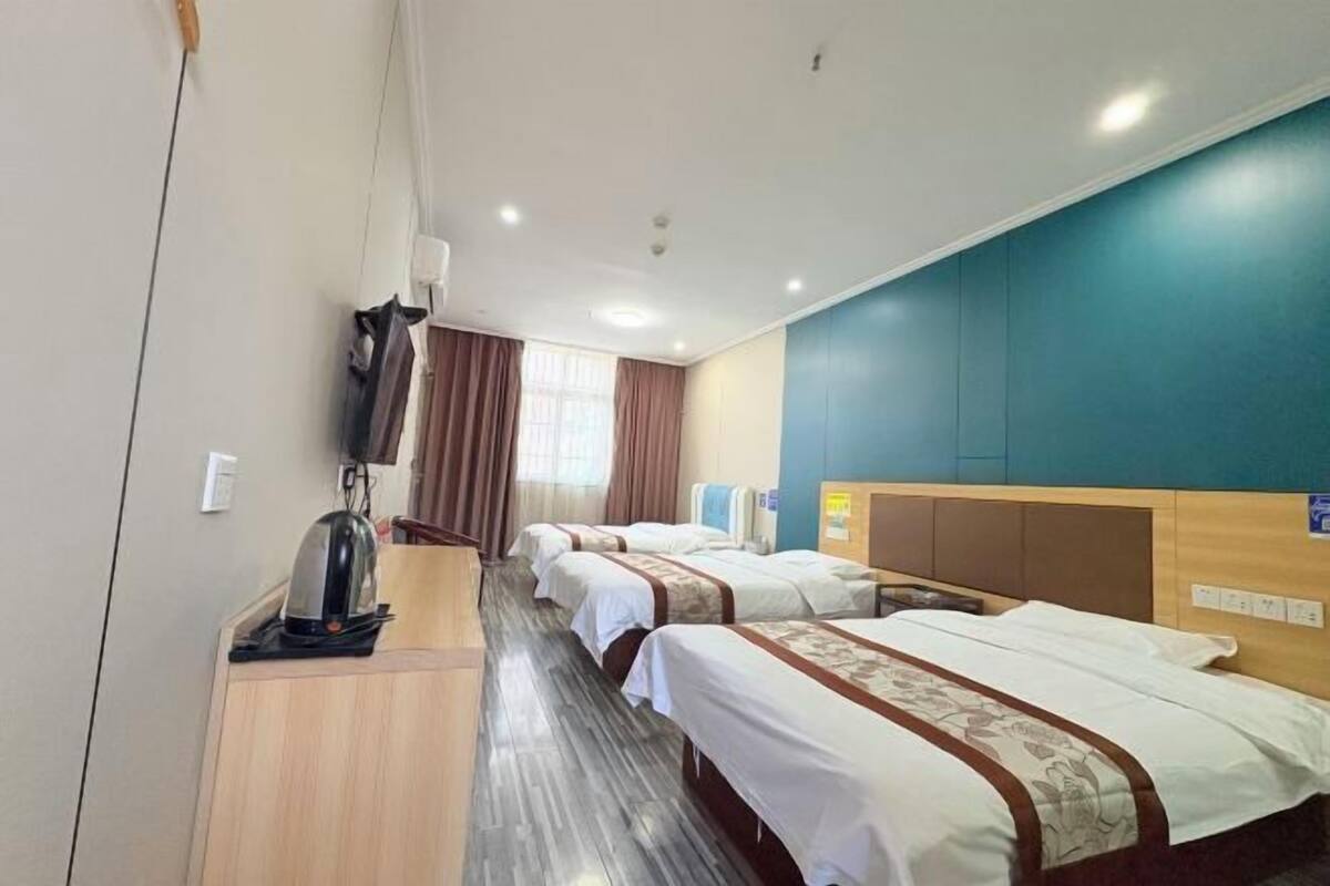 A hotel room with three beds, a wooden desk, a kettle, and a window with curtains.