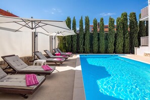 A swimming pool with lounge chairs and umbrellas, surrounded by tall trees. - House Rose With Private Pool And Garden, Pinezići, Croatia (Pinezići)