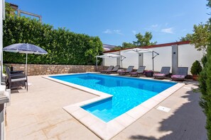 A rectangular swimming pool with a stone border, surrounded by lounge chairs and umbrellas. - House Rose With Private Pool And Garden, Pinezići, Croatia (Pinezići)