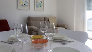 A dining table set with white plates, bowls, and wine glasses, with a sofa and artwork in the background.