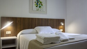 A neatly made bed with white linens and towels, a wooden headboard, and a framed floral artwork on the wall.