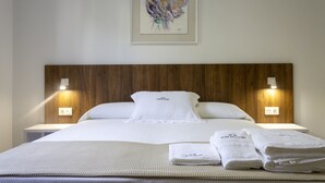 Un lit bien fait, avec du linge de lit blanc, deux lampes de chevet et une œuvre d’art encadrée au-dessus.