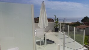 Un balcon moderne avec une balustrade en verre, une table blanche et un pot de fleurs.