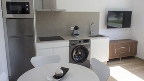 Une cuisine compacte équipée d’un four à micro-ondes, d’une machine à café, d’un évier et d’un lave-linge. On y trouve également une table à manger avec des chaises et un téléviseur fixé au mur.