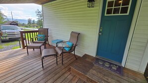 A wooden deck with two chairs and a table, a blue door, and a welcome mat. - Charming 3-bedroom farmhouse 1 hour from Beaver Stadium (Williamsport)
