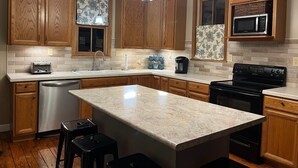 A kitchen with wooden cabinets, a stainless steel dishwasher, a black stove, and a granite island. - Charming 3-bedroom farmhouse 1 hour from Beaver Stadium (Williamsport)