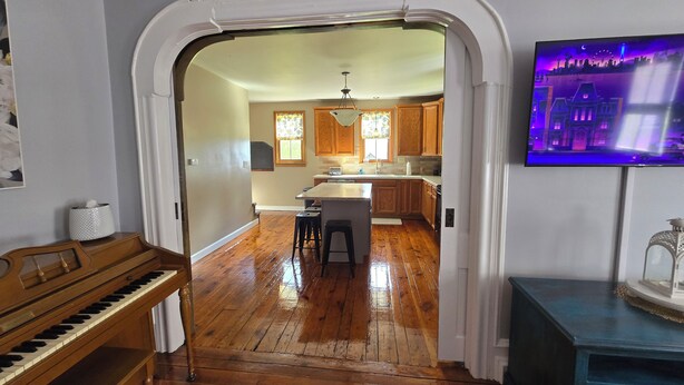 A kitchen with wooden cabinets, a central island, and a television mounted on the wall. - Charming 3-bedroom farmhouse 1 hour from Beaver Stadium (Williamsport)
