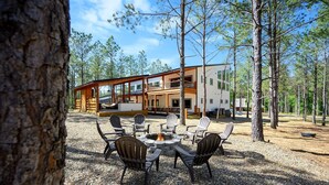 A lodge with a fire pit and Adirondack chairs in front, surrounded by trees.