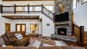A spacious living room with a fireplace, a staircase to an upper level, and a large window.