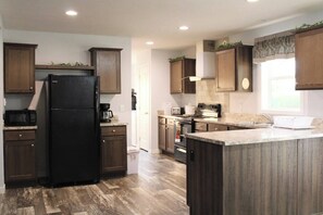 Une cuisine moderne avec des meubles en bois, un réfrigérateur noir, un îlot central intégré et une fenêtre avec des rideaux.