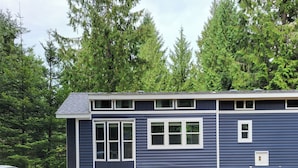 A two-story house with a dark blue exterior, white trim, and multiple windows. - Luxurious quiet cottage on 25 acre rescue farm. In the forest above Port Angeles (Port Angeles)