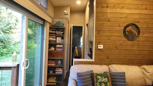 A cozy interior with a wooden wall, a sofa with pillows, a bookshelf, and a door leading to another room. - Luxurious quiet cottage on 25 acre rescue farm. In the forest above Port Angeles (Port Angeles)