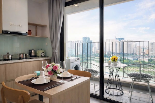 A modern kitchen with a dining area, a washing machine, and a balcony with a city view.