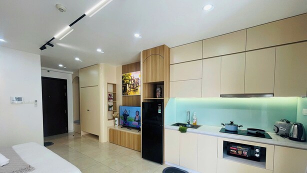 A modern hotel room with a bed, a TV, a kitchen area with a fridge, and a microwave.