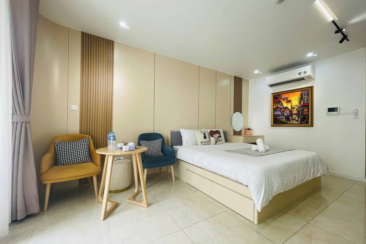 A hotel room with a bed, a desk, two chairs, a small table, and a painting on the wall.