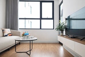 A modern living room with a sofa, a round coffee table, a TV, and a window with blinds.