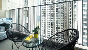 A balcony with two black wicker chairs, a small glass table, a potted plant, and a washing machine.